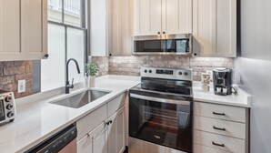 A modern kitchen with white cabinets, a stainless steel microwave, an oven, and a coffee maker. - Beautiful Renovated Apartment Near King Street (Charleston)