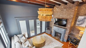 A modern living room with a large window, a fireplace, a television, and a round wooden coffee table. - Beautiful Renovated Apartment Near King Street (Charleston)