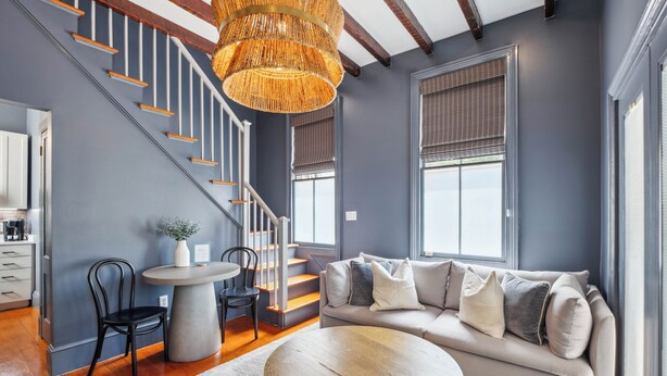 A modern living room with a gray sofa, a round wooden coffee table, and a staircase with wooden railings. - Beautiful Renovated Apartment Near King Street (Charleston)
