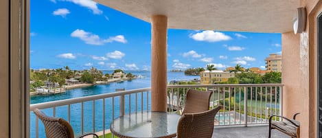 A balcony with a glass table and wicker chairs, overlooking a body of water and a marina.