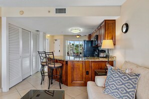 A compact kitchen with a central island, a dining area with chairs, and a sofa with a patterned pillow.
