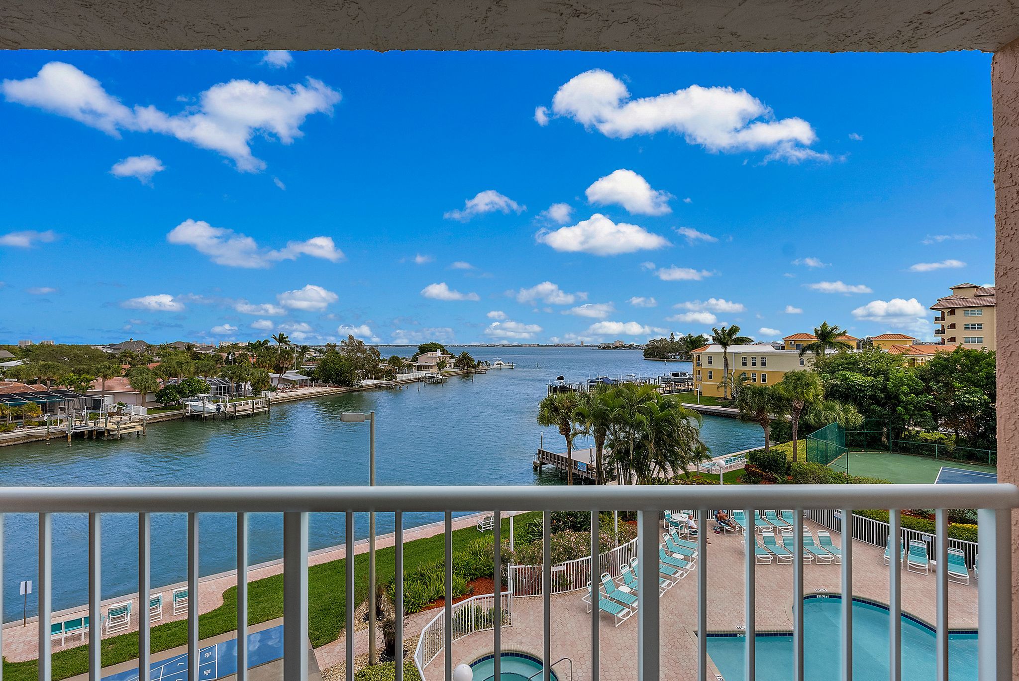 A view from a balcony overlooking a marina with boats, a swimming pool, and a clear blue sky.