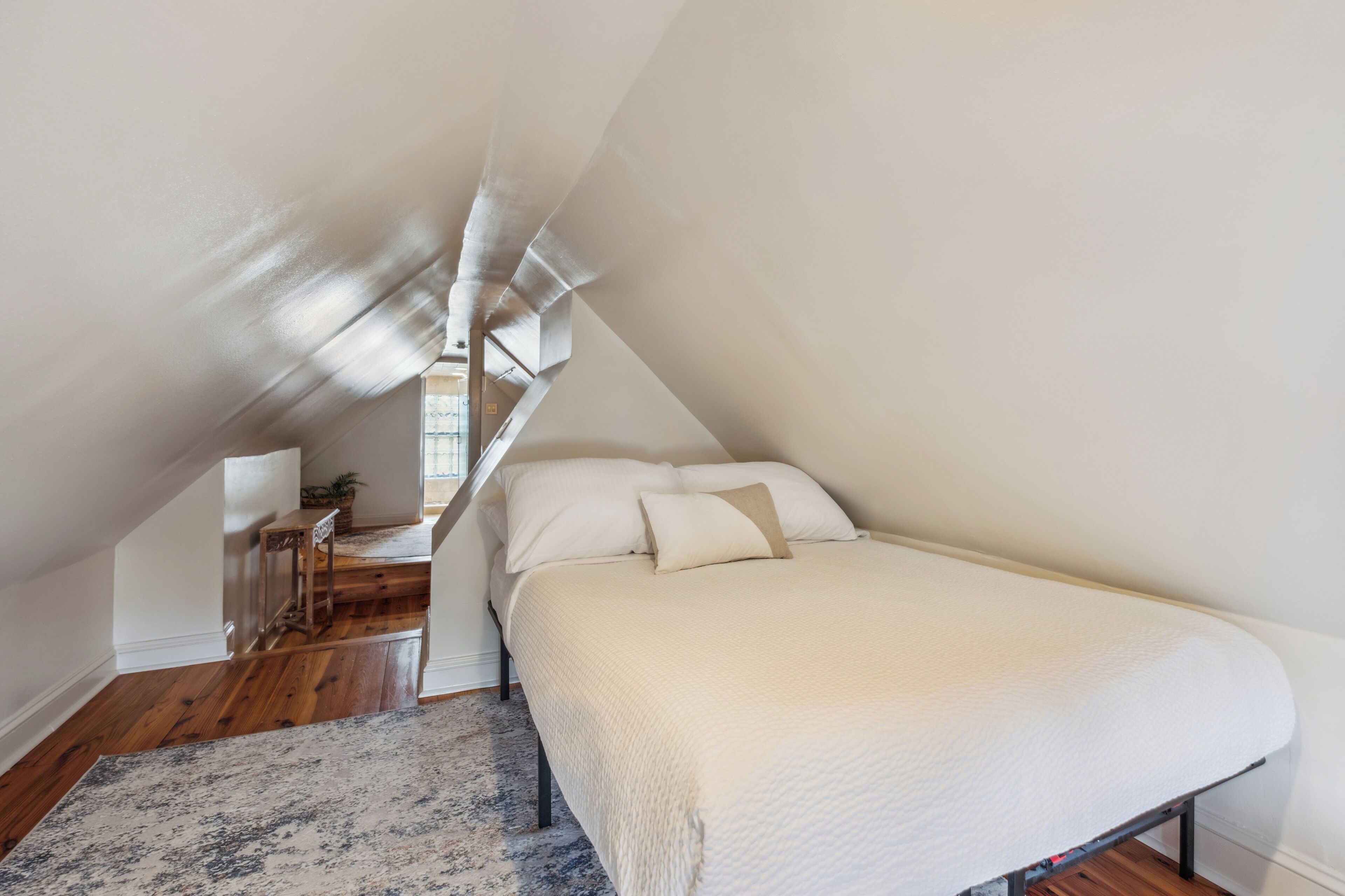 Une chambre avec un plafond en pente, un lit avec une literie blanche, un plancher en bois et une petite table avec une chaise.
