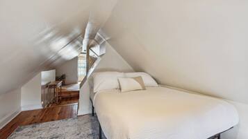 Une chambre avec un plafond en pente, un lit avec une literie blanche, un plancher en bois et une petite table avec une chaise.