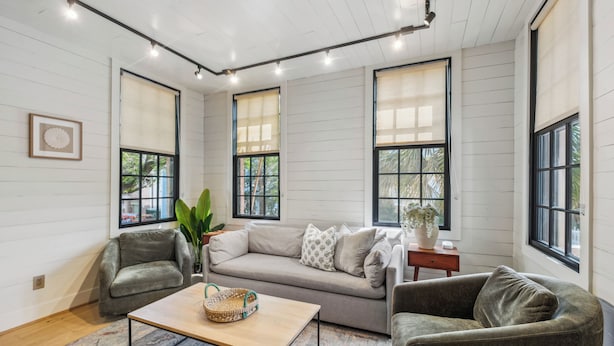 A cozy living room with a sofa, armchairs, a coffee table, and large windows with blinds. - Revitalized Historical Southern Residence (Charleston)