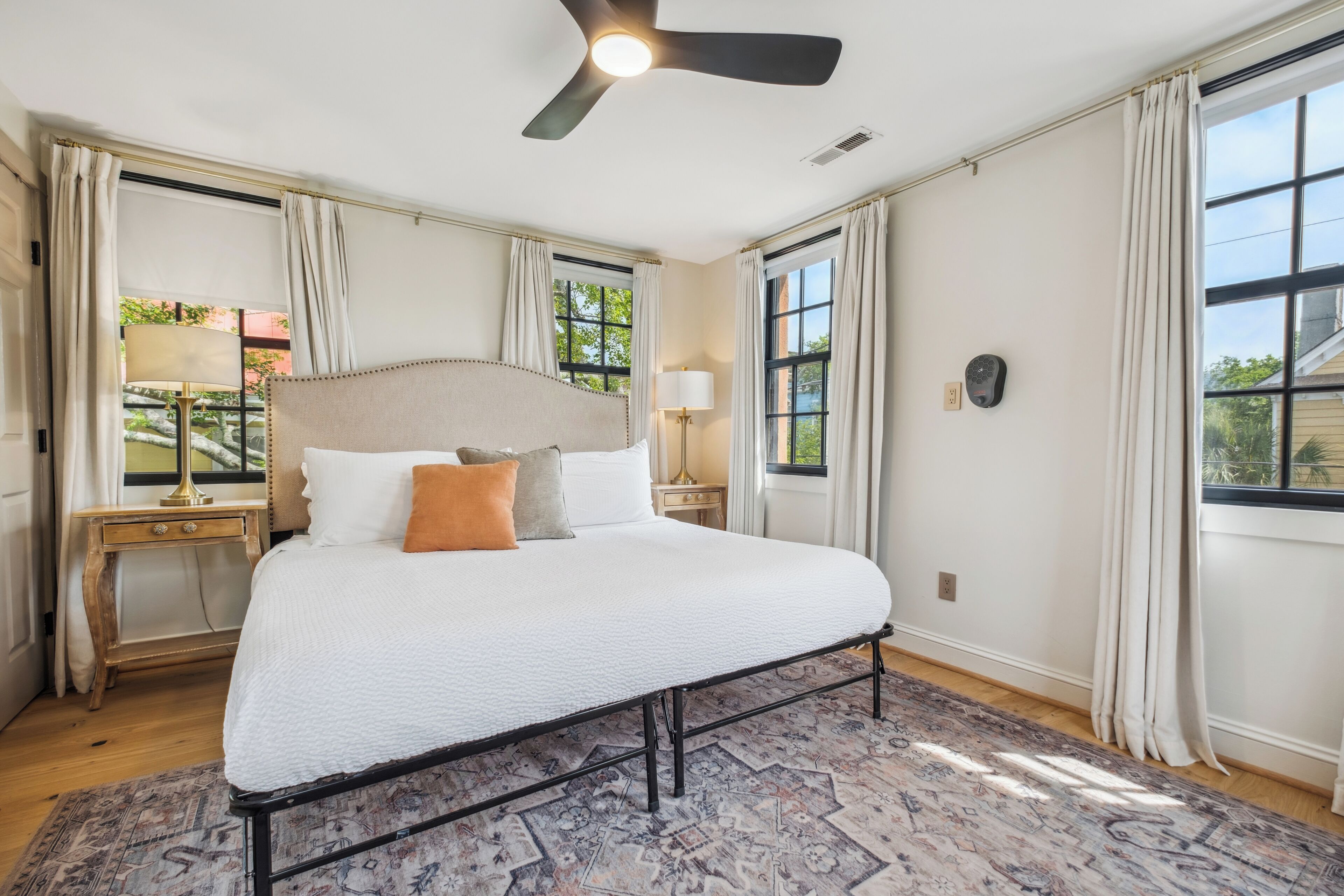 Un grand lit avec une tête de lit, un ventilateur de plafond et un tapis à motifs.