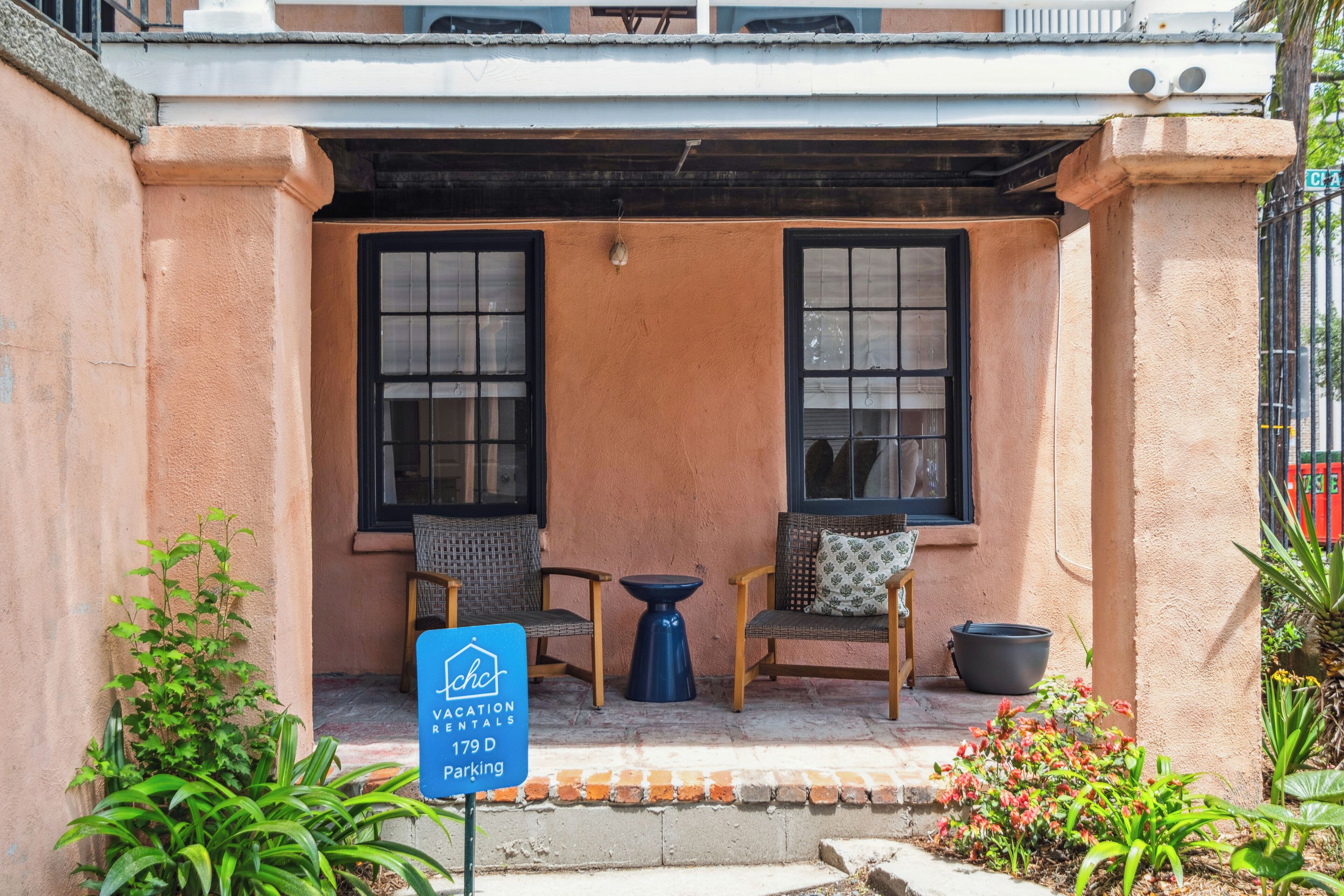 A building with a sign indicating it's a vacation rental. There are two windows, a small table, and two chairs outside.