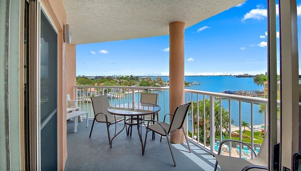 A balcony with a glass table and chairs, overlooking a marina and water body. - Coastal Escape | Pool, Tennis, + Shuffleboard (St. Pete Beach)