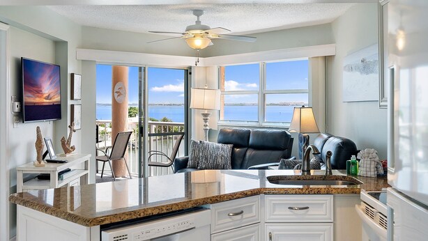 A modern kitchen with a large island, a ceiling fan, and a view of the ocean. - Coastal Escape | Pool, Tennis & Pickleball (St. Pete Beach)