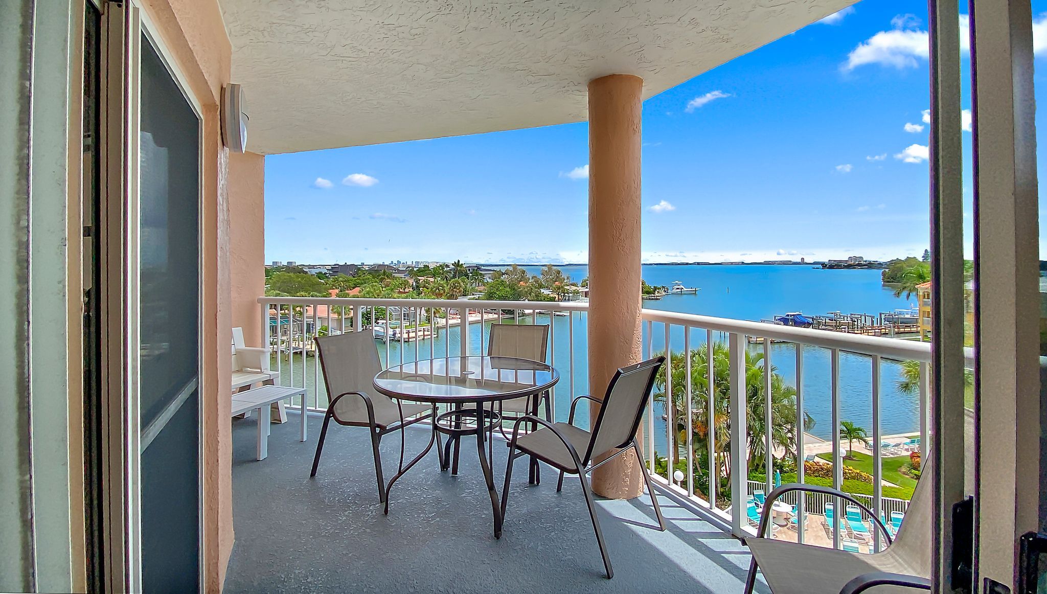 A balcony with a glass table and chairs, overlooking a marina and water body.