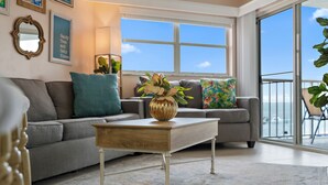 A living room with a sofa, a coffee table, and a view of the sky through large windows. - Sun, Sand & Style | Ideal Beach Retreat (St. Pete Beach)