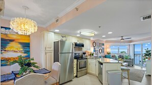 A modern kitchen with stainless steel appliances, a dining area with a table and chairs, and a view of the ocean through large windows. - Sun, Sand & Style | Ideal Beach Retreat (St. Pete Beach)