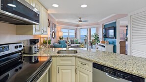 A modern kitchen with granite countertops, stainless steel appliances, and a large window offering a view of the outdoors. - Sun, Sand & Style | Ideal Beach Retreat (St. Pete Beach)