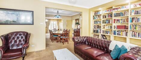 A living room with a red leather sofa, a matching armchair, a marble coffee table, and a bookshelf filled with books.