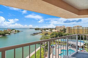 A balcony with a view of a marina, a swimming pool, and hotel buildings. - Bayside Luxury Condo | Amazing Views | Amenities (St. Pete Beach)