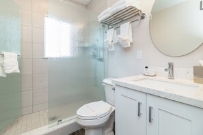 Casa de banho moderna com cabine de duche de vidro, sanita, lavatório com bancada de mármore e espelho redondo.