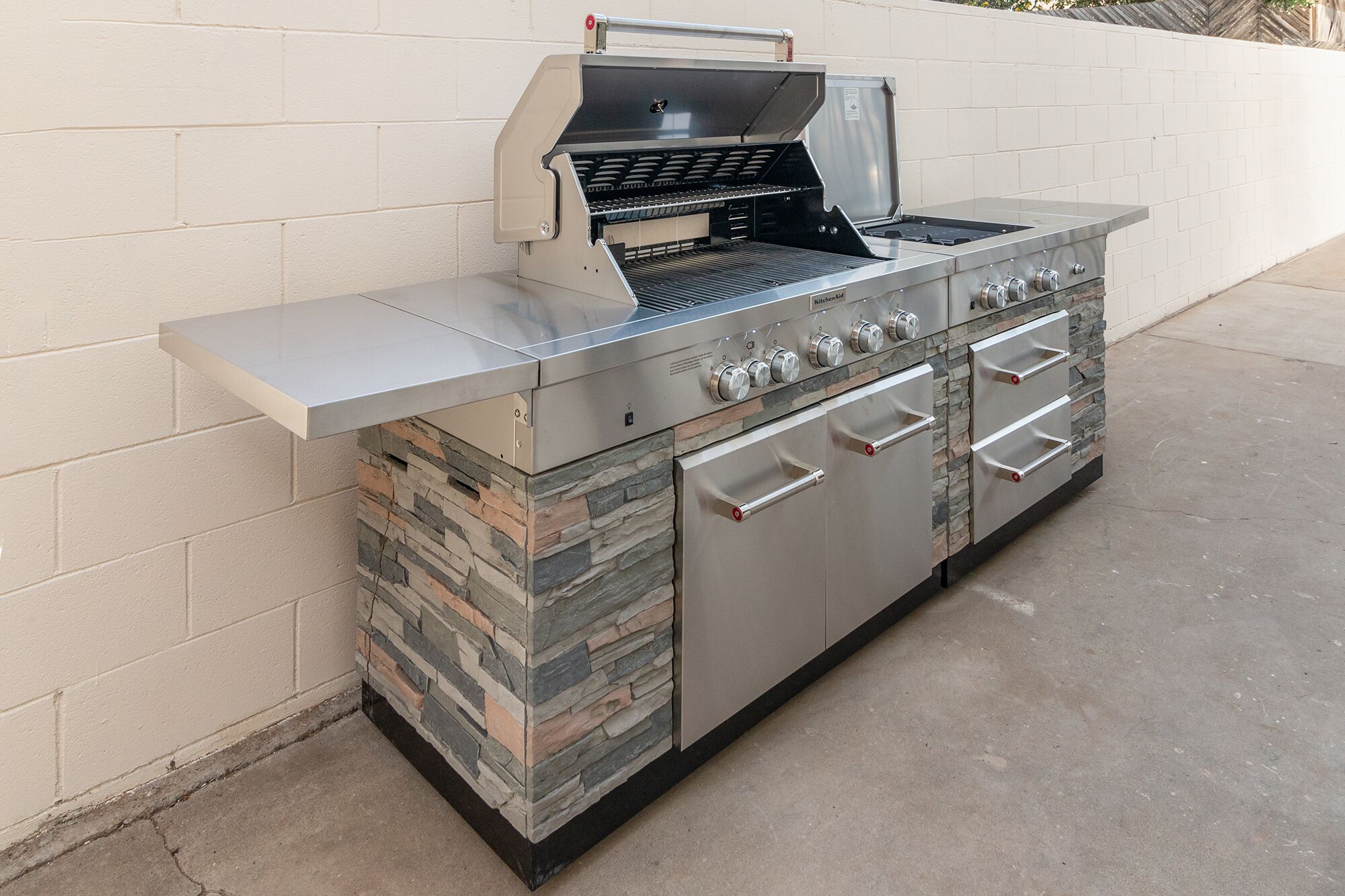 Cocina exterior de acero inoxidable con una parrilla, varios fogones y un lavaplatos integrado.