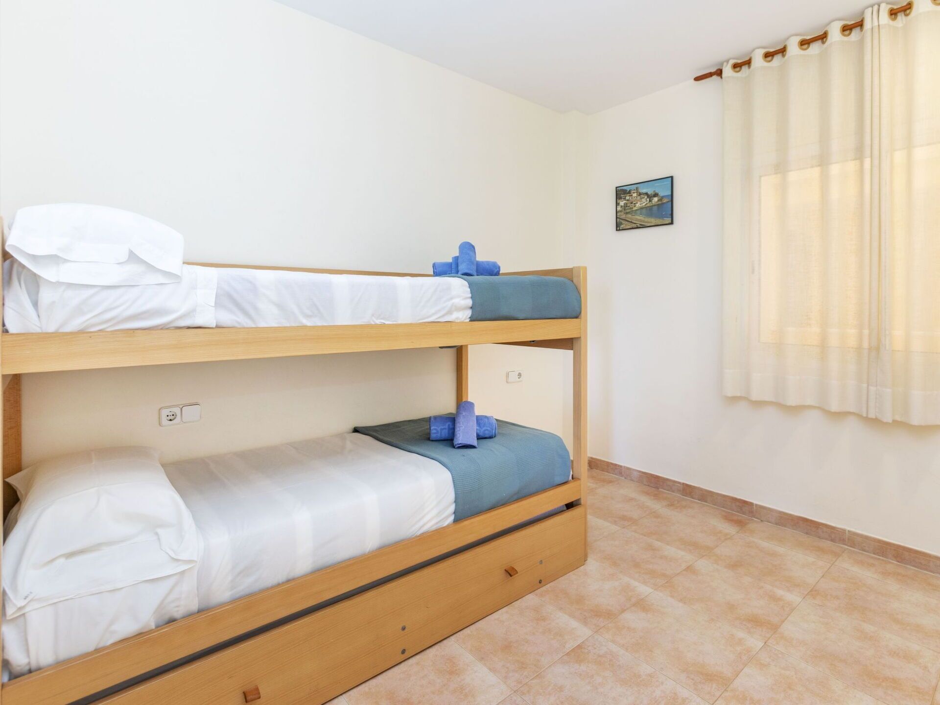 A bunk bed room with a small painting on the wall and a curtain on the window.