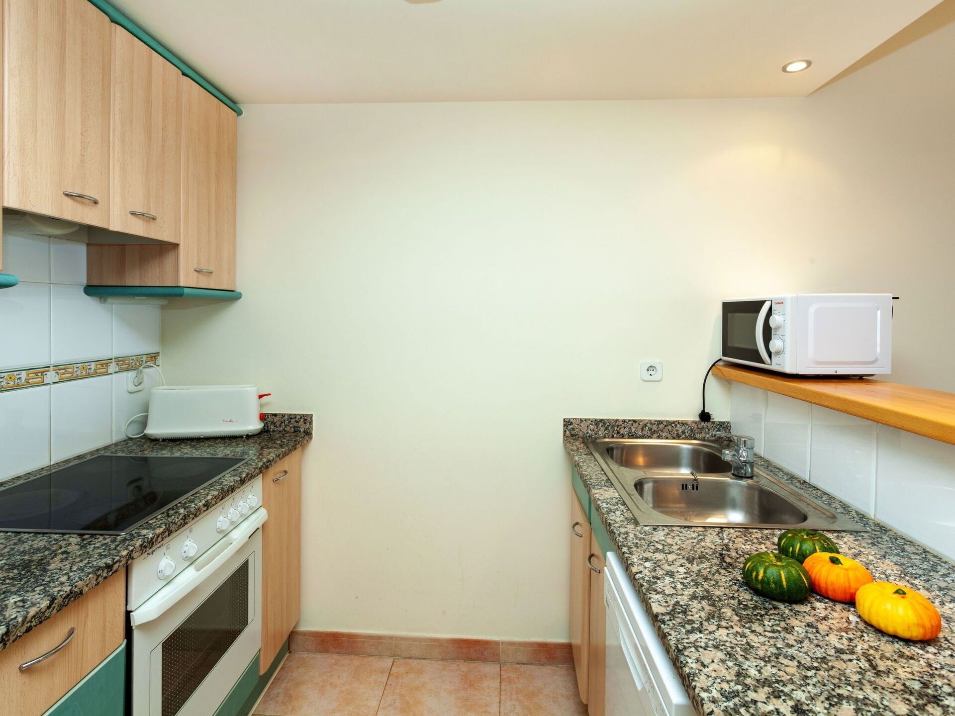 Una cucina compatta con piano cottura, forno a microonde, lavello e ripiani in granito.