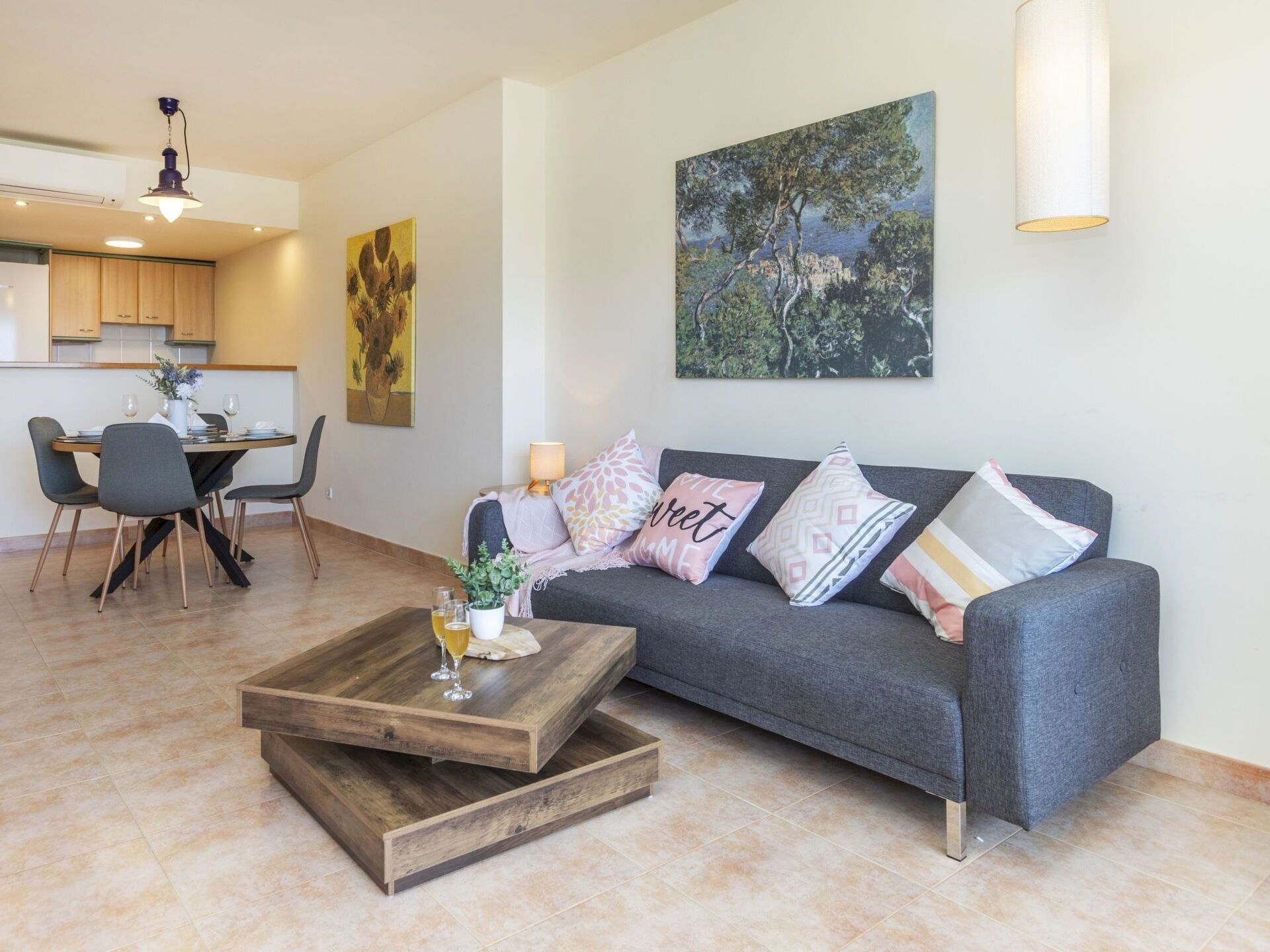 Een moderne woonkamer met een grijze bank, een houten salontafel en een eethoek met een tafel en stoelen.