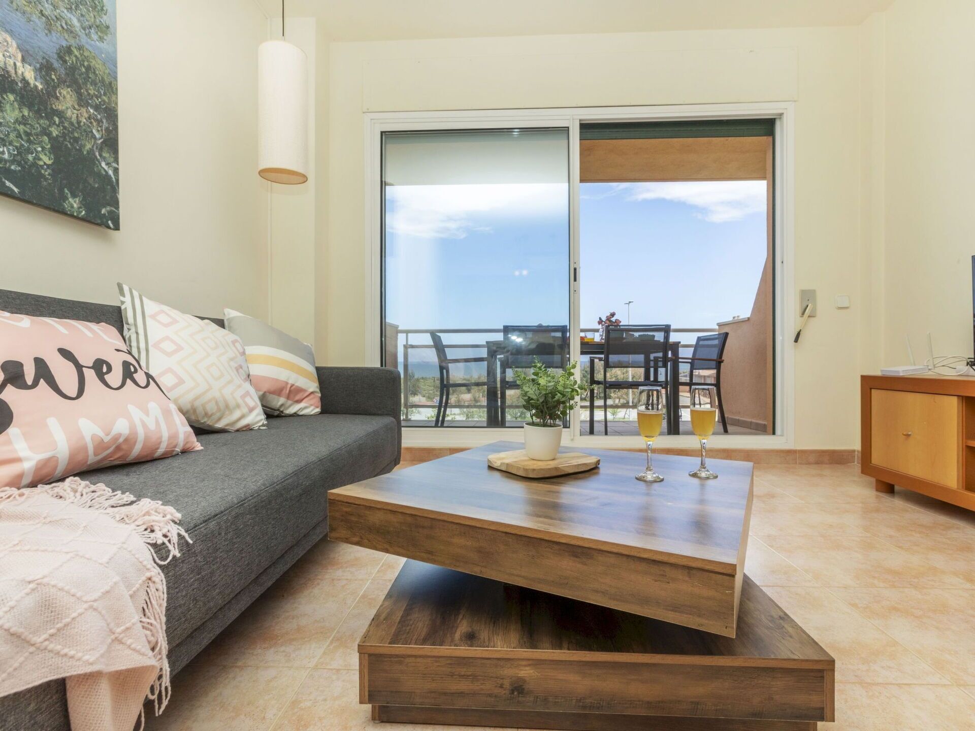 A living room with a grey sofa, a wooden coffee table, and a balcony with a table and chairs.