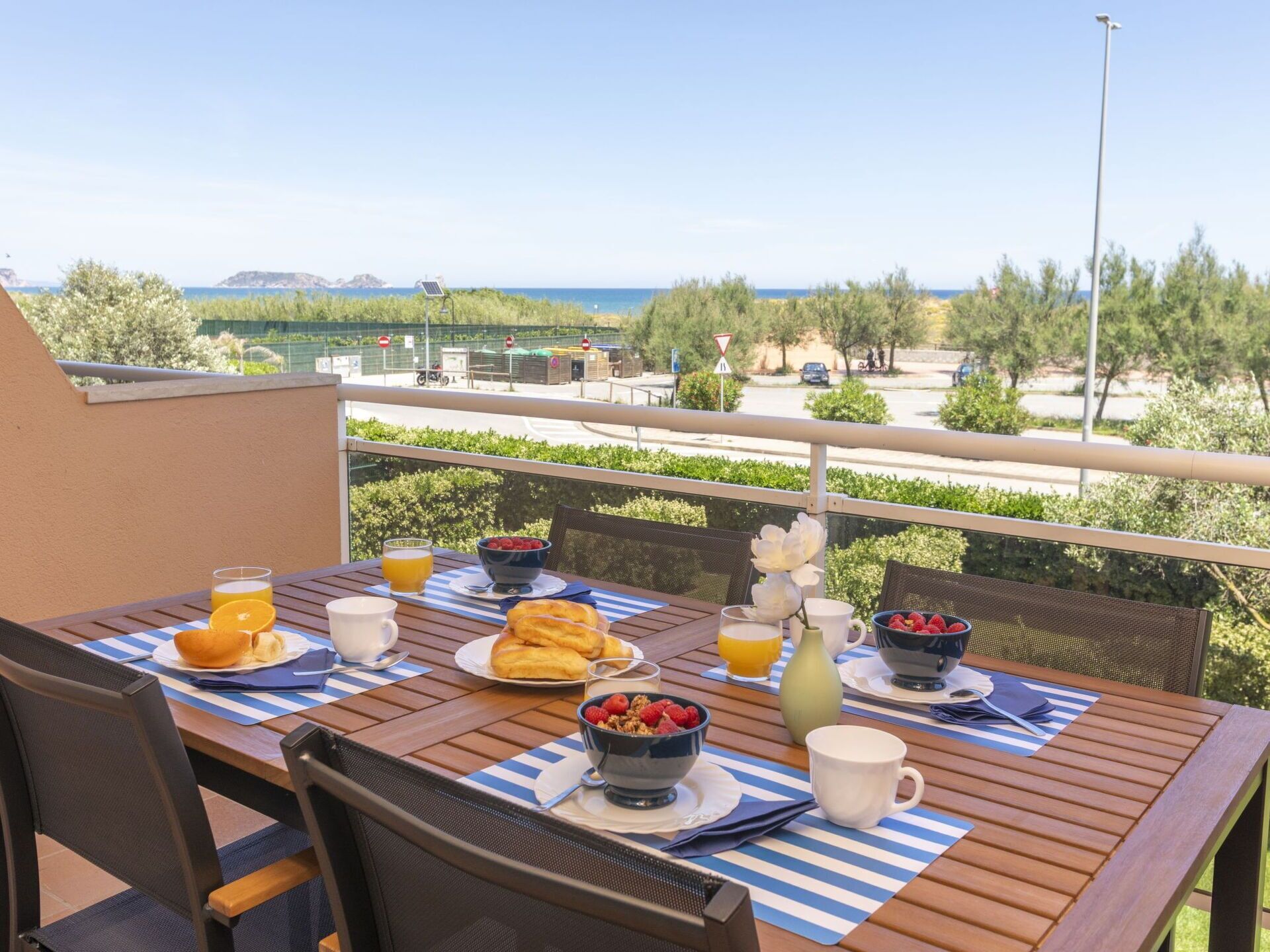 A balcony with a table set for breakfast, overlooking a coastal view.