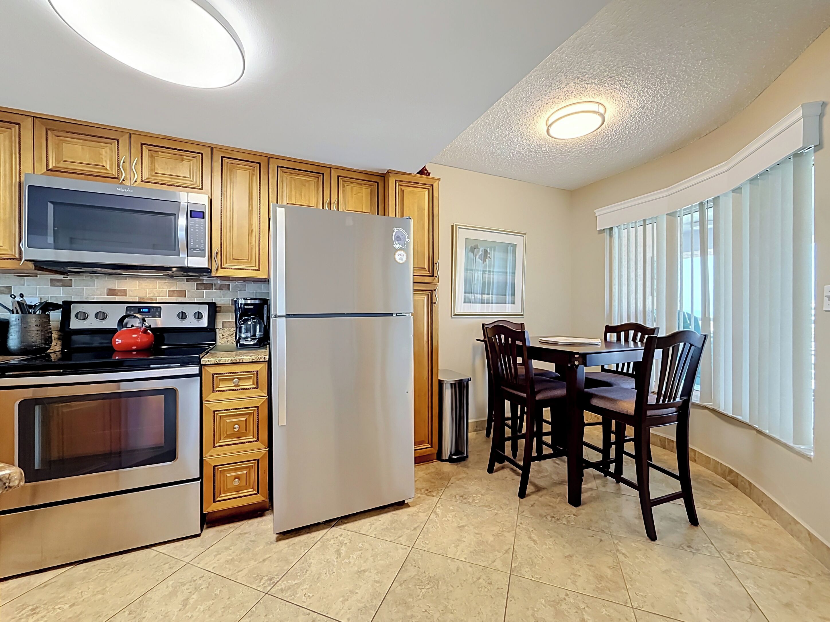 A kitchen with wooden cabinets, a stainless steel refrigerator, a microwave, an oven, and a dining area with a table and chairs.