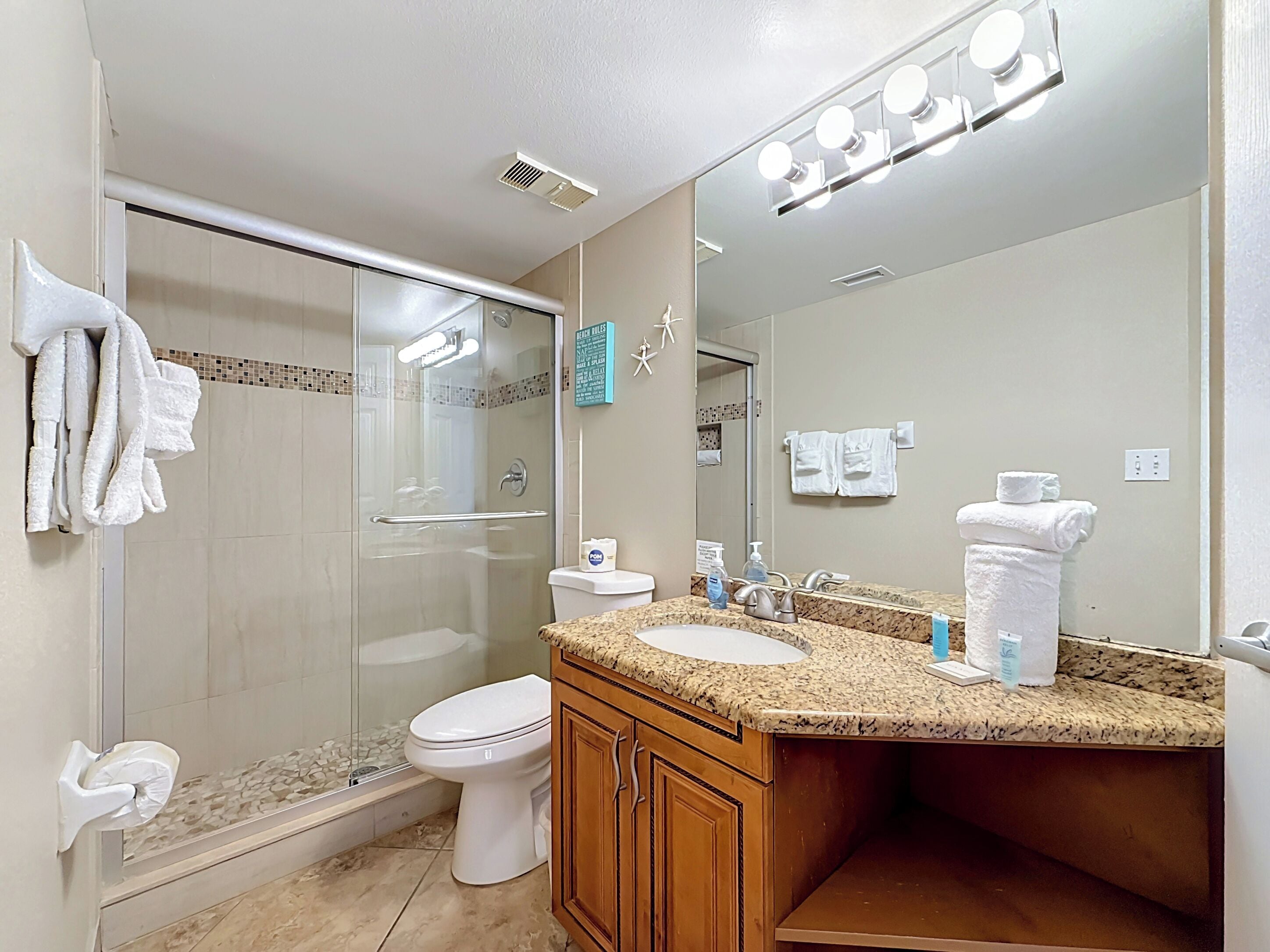 A bathroom with a glass shower enclosure, a toilet, a sink with a mirror, and towels.