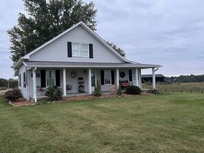 Une maison de plain-pied avec un porche, une pelouse devant et un paysage en arrière-plan.