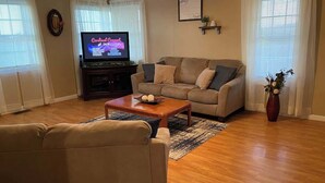 A living room with a sofa, a coffee table, a television, and a vase with flowers. - Beautiful Farmhouse near Lake Cumberland (Monticello)