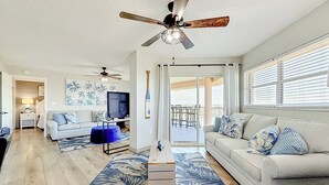 Un salon spacieux doté d’un ventilateur de plafond, d’un téléviseur et offrant une vue sur l’extérieur.