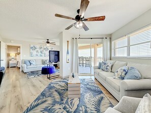 A spacious living room with a ceiling fan, a television, and a view to the outside.