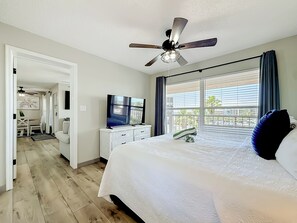 Une chambre d’hôtel équipée d’un lit, d’une télévision, d’un ventilateur de plafond et d’une fenêtre avec des stores.