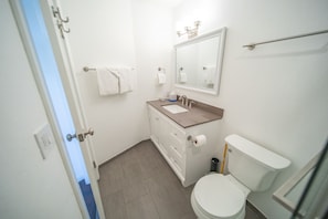 A small bathroom with a toilet, sink, and mirror. There are towels hanging on the wall and a door leading to another room. - Mall 1423 (Keystone)