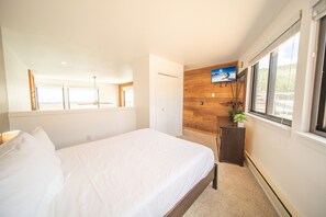 A bedroom with a large bed, a wooden accent wall, a small desk, and a window with a view. - Mall 1423 (Keystone)
