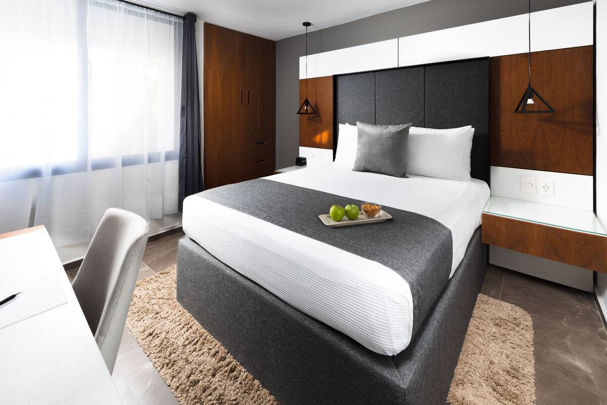 A modern hotel room with a large bed, a desk, and a chair.