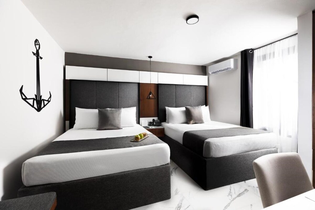 A modern hotel room with two beds, a nightstand, a wall-mounted light, and a window with curtains.