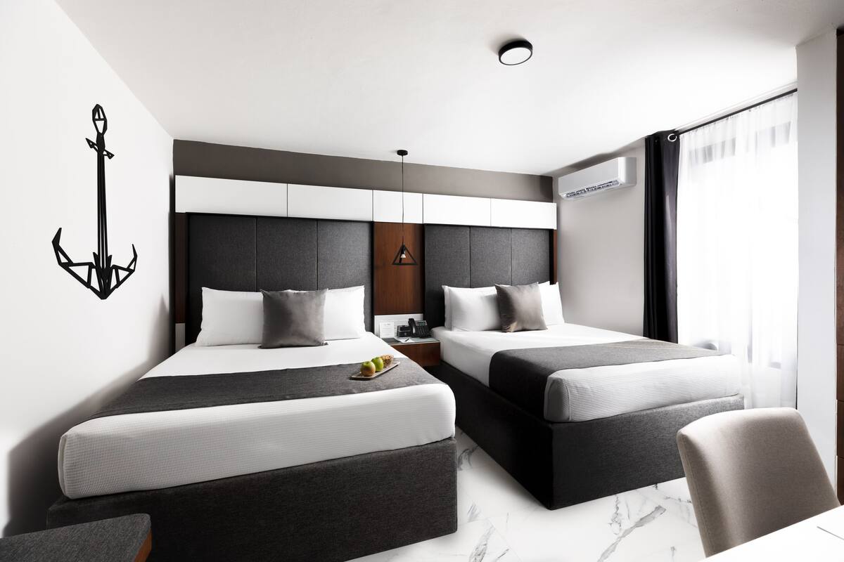 A modern hotel room with two beds, a nightstand, a wall-mounted lamp, and a window with curtains.