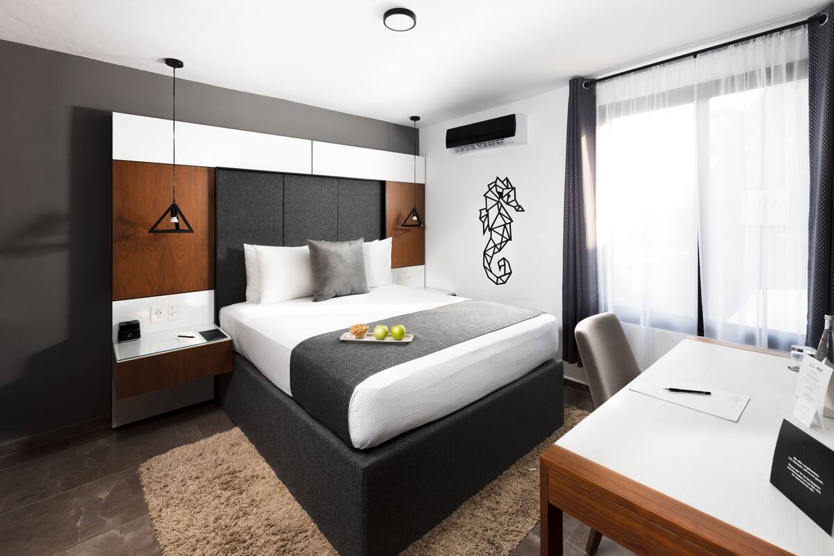 A modern hotel room with a large bed, bedside tables, a desk, and a view of the outdoors.
