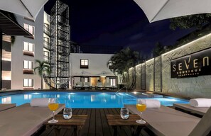 Et poolområde med liggestole, et bardisk og et skilt med teksten 'SEVEN BOUTIQUE APARTMENTS'.