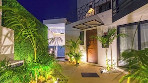 A modern building with a well-lit entrance, a green wall, and a pathway leading to the door.