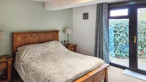 Une chambre à coucher avec un lit en bois, une table de chevet, une lampe et une vue sur la verdure par une porte.