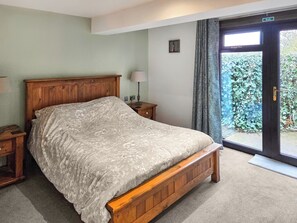 A bedroom with a wooden bed, a nightstand, a lamp, and a view of greenery through a door. - 1 bedroom accommodation in Annan, near Dumfries (Annan, near Dumfries)