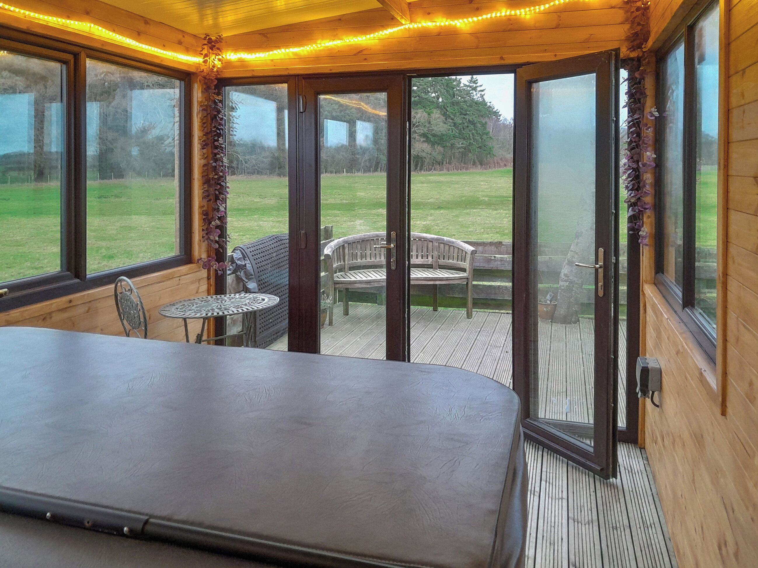 A room with a large bed, a small table, and chairs, with a view of a grassy area through glass doors.