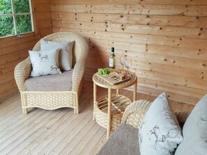 A wicker chair with cushions, a small round table with a bottle and glasses, and a view through a window. - 1 bedroom accommodation in Annan, near Dumfries (Annan, near Dumfries)