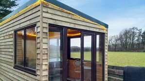 Une cabane en bois dotée de grandes portes vitrées, d’une terrasse en bois et offrant une vue sur un champ verdoyant.