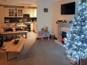 A living room with a fireplace, a Christmas tree, and a kitchen in the background. - 1 bedroom accommodation in Annan, near Dumfries (Annan, near Dumfries)