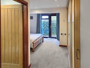 Quarto com cama, porta, janela com cortinas e vista para o verde lá fora.