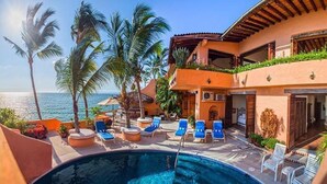 A poolside area with lounge chairs, a swimming pool, and a view of the ocean.