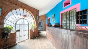 Un área de recepción con pared de ladrillo, ventanas arqueadas y una paleta de colores azul y rosa.